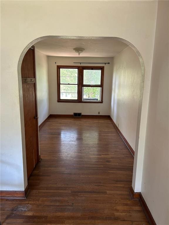 empty room featuring arched walkways, dark wood-style flooring, and baseboards