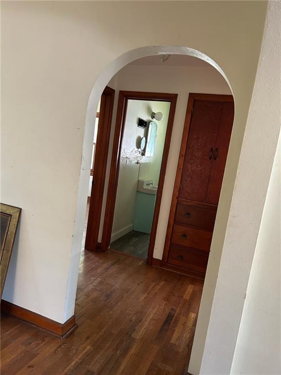 corridor with arched walkways, dark wood finished floors, and baseboards