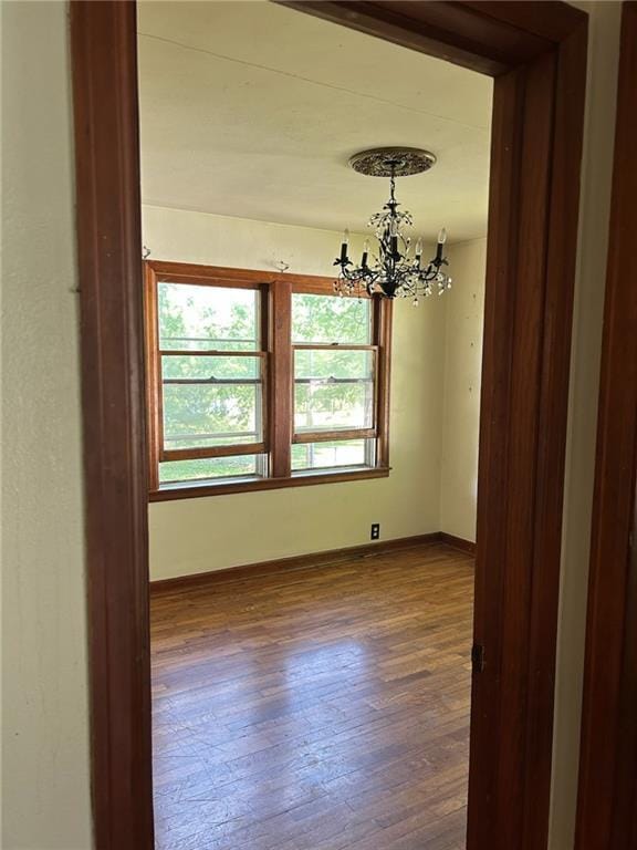 empty room with a chandelier, dark wood-style flooring, and baseboards