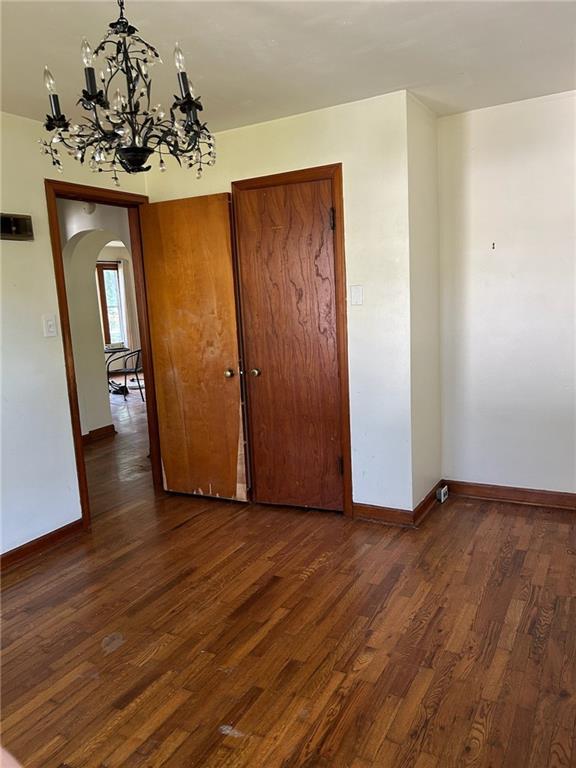 spare room featuring arched walkways, dark wood finished floors, a chandelier, and baseboards