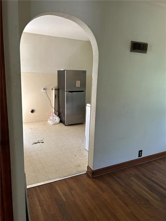 corridor with arched walkways, wood finished floors, and baseboards