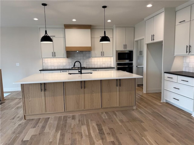 9019 Freedom Cir, Lenexa, KS 66227 - kitchen with oven, a sink, light wood-type flooring, tasteful backsplash, and a center island with sink