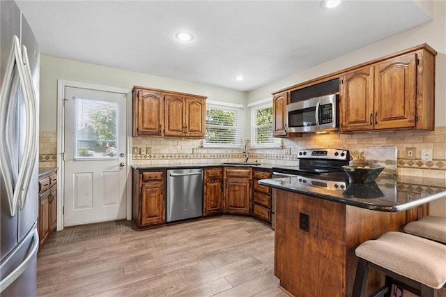 21607 W 51st St, Shawnee, KS 66226 - kitchen featuring appliances with stainless steel finishes, a peninsula, brown cabinets, light wood-type flooring, and decorative backsplash