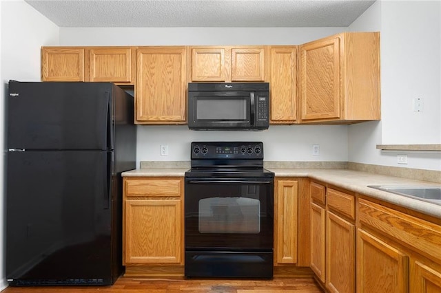 5412 Fairmount Ave, Kansas City, MO 64118 - kitchen with black appliances, light countertops, wood finished floors, and a textured ceiling