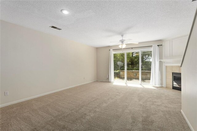 5412 Fairmount Ave, Kansas City, MO 64118 - unfurnished living room with light carpet, a ceiling fan, a tiled fireplace, a textured ceiling, and baseboards