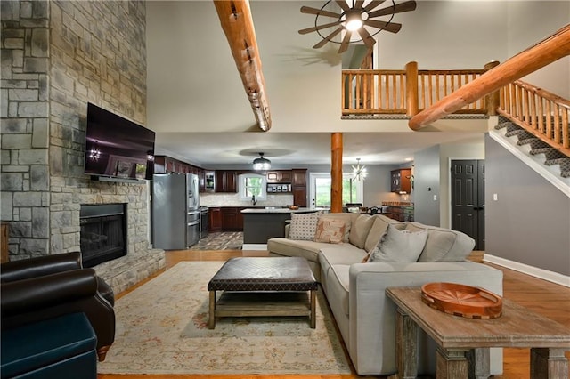 611 N Winnebago Dr, Lake Winnebago, MO 64034 - living room featuring ceiling fan, a stone fireplace, light wood-style floors, stairs, and a high ceiling