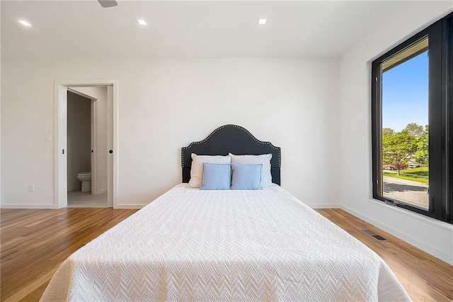 bedroom featuring wood finished floors, baseboards, and ensuite bathroom