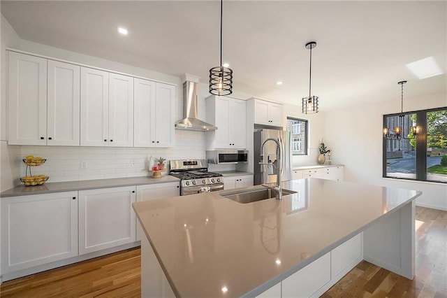 2605 W Paseo Blvd, Kansas City, MO 64108 - kitchen with stainless steel appliances, wall chimney range hood, a center island with sink, decorative backsplash, and light wood-style flooring