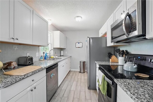 10621 E 32nd St, Independence, MO 64052 - kitchen featuring stainless steel appliances, a sink, light wood-style floors, white cabinetry, and backsplash