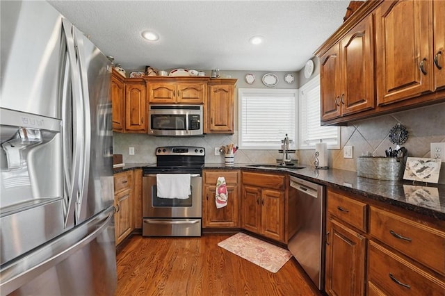1037 NW 91st Ter, Kansas City, MO 64155 - kitchen featuring stainless steel appliances, a sink, dark wood-style floors, brown cabinetry, and a textured ceiling