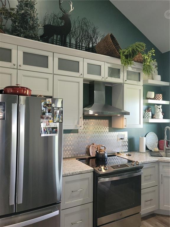 1154 SE 364p Rd, Clinton, MO 64735 - kitchen featuring stainless steel appliances, wall chimney exhaust hood, open shelves, decorative backsplash, and lofted ceiling
