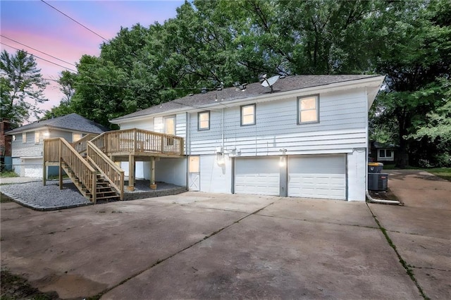 8823 E 111th St, Kansas City, MO 64134 - back of property at dusk with an attached garage, driveway, a wooden deck, and stairway
