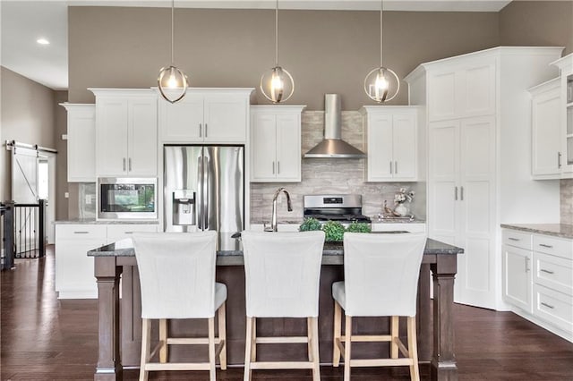 8756 Houston St, Lenexa, KS 66227 - kitchen with appliances with stainless steel finishes, wall chimney exhaust hood, a kitchen island with sink, backsplash, and dark wood-type flooring