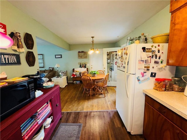 310 E Monroe Ave, Garnett, KS 66032 - kitchen featuring black microwave, freestanding refrigerator, dark wood-style flooring, light countertops, and a chandelier
