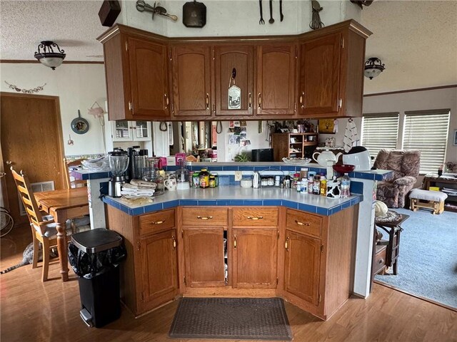 476 170th St, Fort Scott, KS 66701 - kitchen with a textured ceiling, tile countertops, wood finished floors, crown molding, and brown cabinetry
