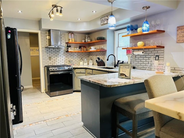 13106 E 57th St, Kansas City, MO 64133 - kitchen with wall chimney range hood, stainless steel gas stove, freestanding refrigerator, a sink, and a peninsula