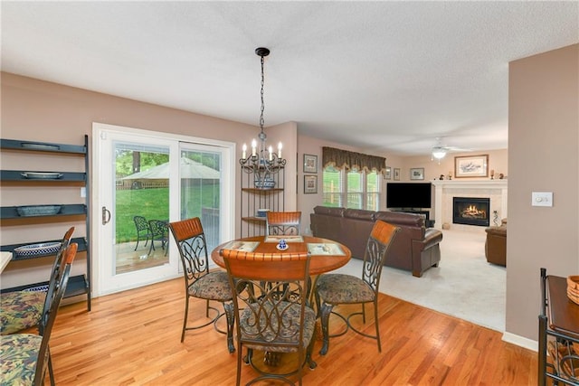 800 Ash Ct, Lansing, KS 66043 - dining room with light wood-style flooring, ceiling fan, a lit fireplace, a chandelier, and a textured ceiling