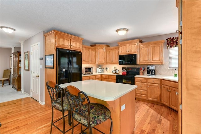 800 Ash Ct, Lansing, KS 66043 - kitchen with black appliances, light countertops, a kitchen breakfast bar, light wood-style floors, and a kitchen island