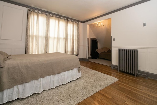 1017 Angelique St, Saint Joseph, MO 64501 - bedroom featuring radiator heating unit, a chandelier, a decorative wall, wood finished floors, and crown molding