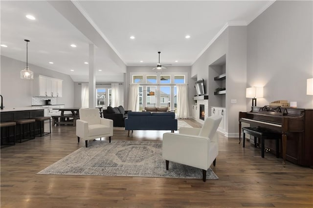 2055 NW Obrien Rd, Lees Summit, MO 64081 - living room featuring ceiling fan, crown molding, recessed lighting, dark wood finished floors, and a warm lit fireplace