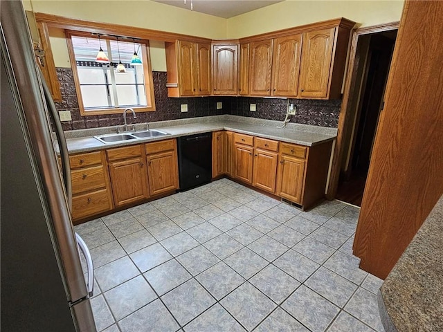 kitchen featuring black dishwasher, a sink, freestanding refrigerator, light tile patterned floors, and tasteful backsplash