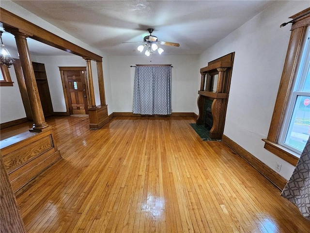 unfurnished living room with a ceiling fan, light wood-type flooring, decorative columns, and baseboards