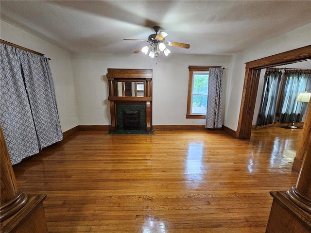 unfurnished living room with wood finished floors, a ceiling fan, a fireplace with flush hearth, and baseboards