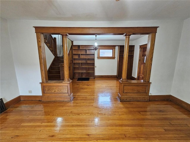 unfurnished living room with wood-type flooring, decorative columns, baseboards, and stairway
