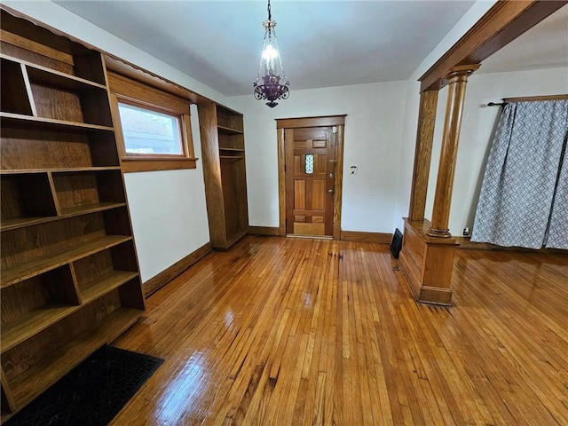 foyer featuring decorative columns, hardwood / wood-style flooring, baseboards, and a chandelier