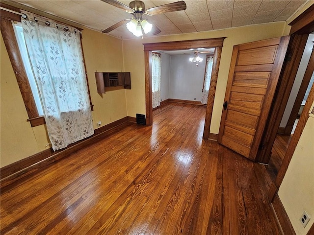 unfurnished room with dark wood finished floors, ceiling fan, baseboards, and a wall unit AC