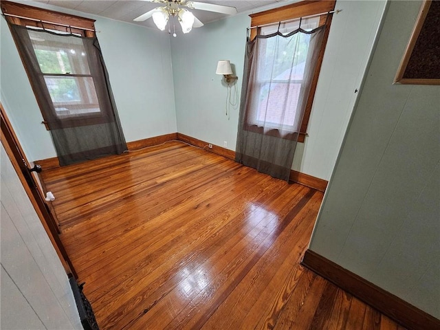 unfurnished room featuring wood-type flooring, a ceiling fan, baseboards, and plenty of natural light