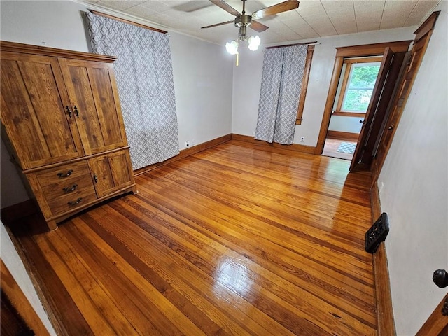 spare room featuring a ceiling fan, wood finished floors, baseboards, and crown molding