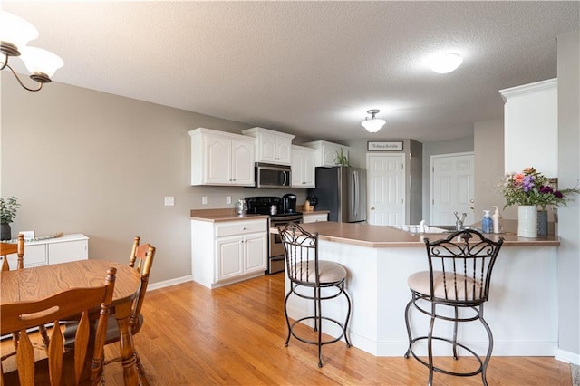 3100 Clarendon Rd, Sedalia, MO 65301 - kitchen featuring appliances with stainless steel finishes, a peninsula, a kitchen bar, white cabinets, and light wood finished floors