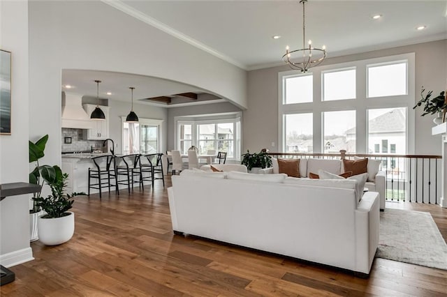 15670 W 165th Ter, Olathe, KS 66062 - living room with arched walkways, a chandelier, recessed lighting, dark wood-style flooring, and crown molding