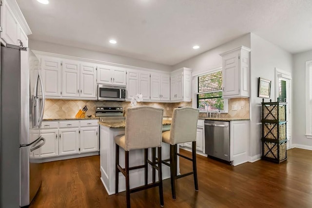 11304 W 144th St, Overland Park, KS 66221 - kitchen with stainless steel appliances, a center island, white cabinetry, light stone counters, and dark wood-style floors