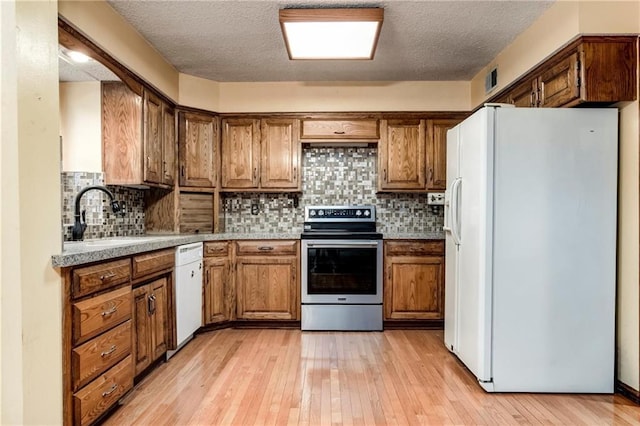 10404 Flint St, Overland Park, KS 66214 - kitchen with white appliances, a sink, light wood finished floors, brown cabinets, and backsplash