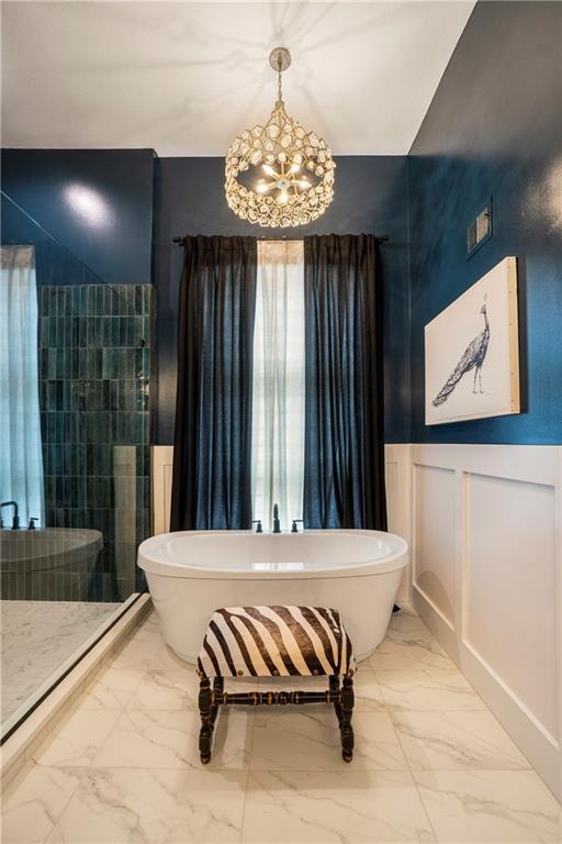 4112 W 156th St, Overland Park, KS 66224 - bathroom with marble look tiles, a chandelier, a freestanding tub, and a wainscoted wall
