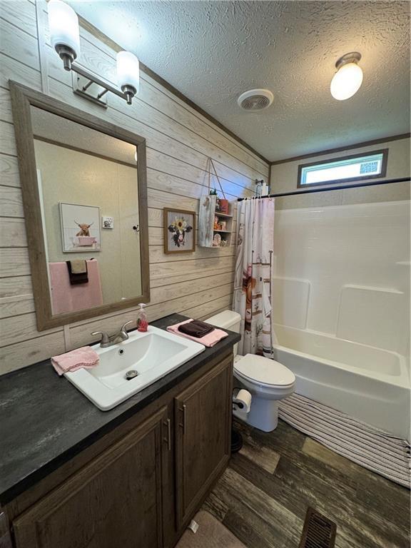 516 E 614th St, Girard, KS 66743 - bathroom with wood finished floors, wood walls, toilet, shower / bath combo, and a textured ceiling