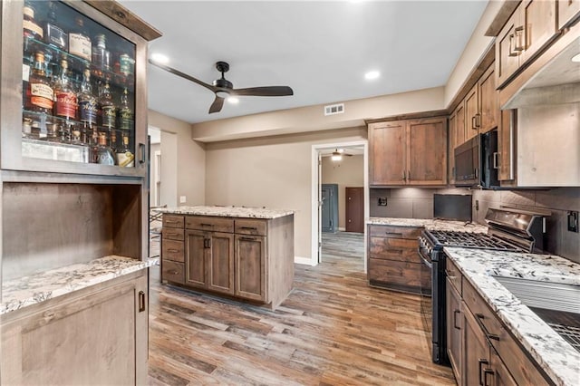 1105 S Gordon St, Concordia, MO 64020 - kitchen featuring stainless steel range with gas stovetop, black microwave, ceiling fan, light wood-style flooring, and tasteful backsplash