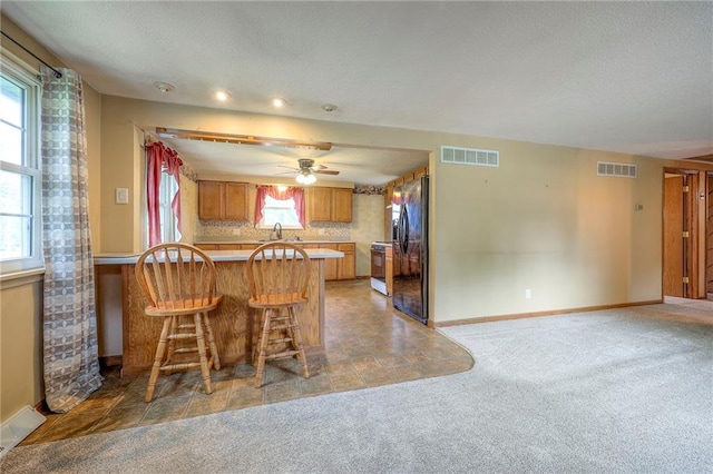 8713 Old Stagecoach Rd, Kansas City, MO 64154 - kitchen featuring gas range, a peninsula, brown cabinetry, light carpet, and black refrigerator with ice dispenser