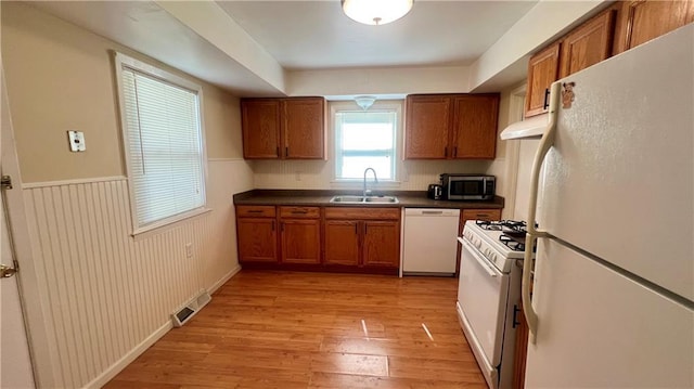 1445 E 77th St, Kansas City, MO 64131 - kitchen with white appliances, brown cabinetry, dark countertops, under cabinet range hood, and light wood-style floors