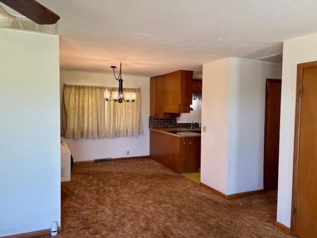 22025 Ness Rd, Parsons, KS 67357 - kitchen featuring brown cabinetry, dark carpet, a chandelier, baseboards, and decorative light fixtures