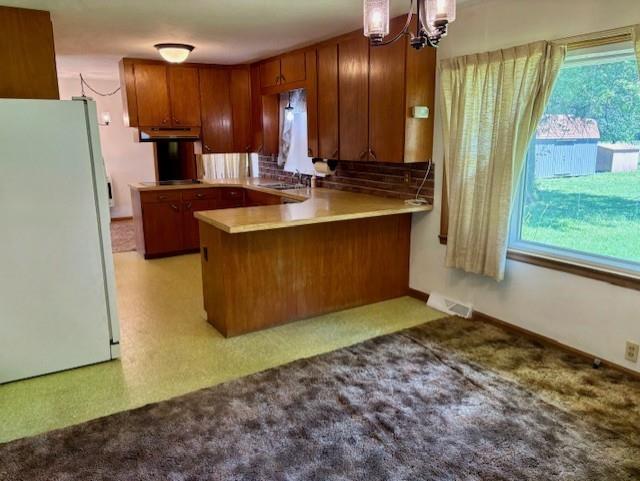22025 Ness Rd, Parsons, KS 67357 - kitchen with freestanding refrigerator, brown cabinets, a peninsula, a chandelier, and light colored carpet