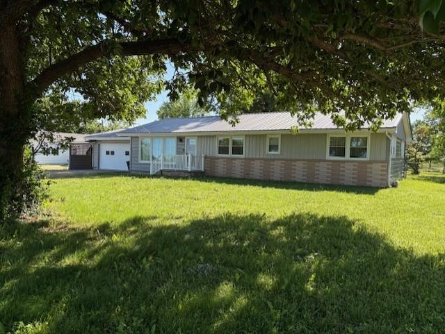 22025 Ness Rd, Parsons, KS 67357 - view of front of house featuring an attached garage, brick siding, a front lawn, and board and batten siding
