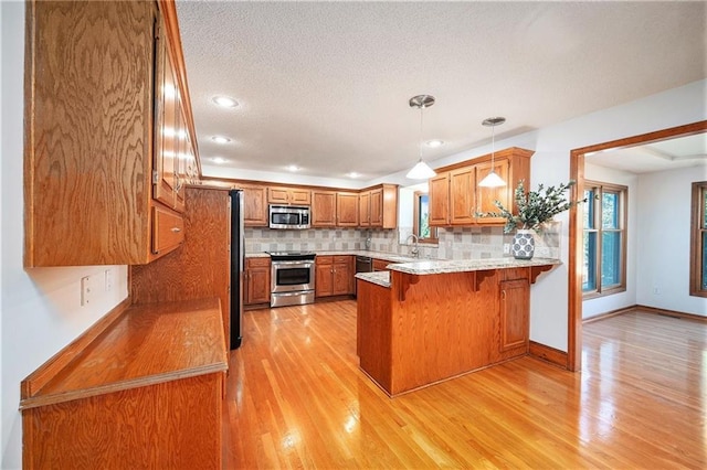 3304 Tepee Ct, Independence, MO 64057 - kitchen with appliances with stainless steel finishes, a peninsula, brown cabinetry, backsplash, and light wood-style floors