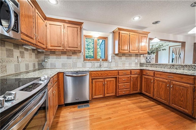 3304 Tepee Ct, Independence, MO 64057 - kitchen featuring appliances with stainless steel finishes, a sink, a textured ceiling, light wood-style floors, and brown cabinets