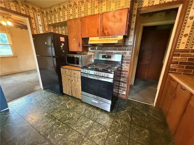 316 N 18th St, Lexington, MO 64067 - kitchen with stainless steel appliances, under cabinet range hood, a ceiling fan, wallpapered walls, and brown cabinetry
