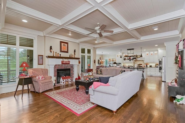 10309 S Oakcrest Ln, Olathe, KS 66061 - living room featuring a ceiling fan, dark wood-type flooring, coffered ceiling, a brick fireplace, and beam ceiling