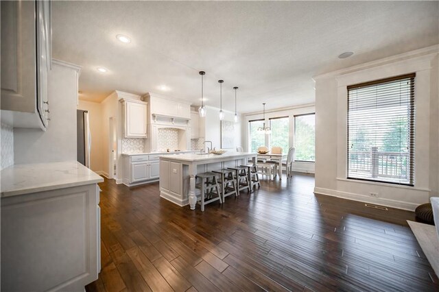 9101 W 158th St, Overland Park, KS 66221 - kitchen featuring a kitchen island with sink, a breakfast bar, dark wood-style flooring, backsplash, and baseboards