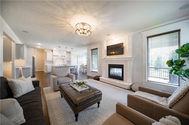 9101 W 158th St, Overland Park, KS 66221 - living room featuring wood finished floors, crown molding, a chandelier, a glass covered fireplace, and baseboards